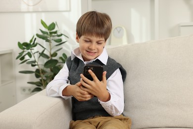 Photo of Cute little boy using smartphone on sofa at home