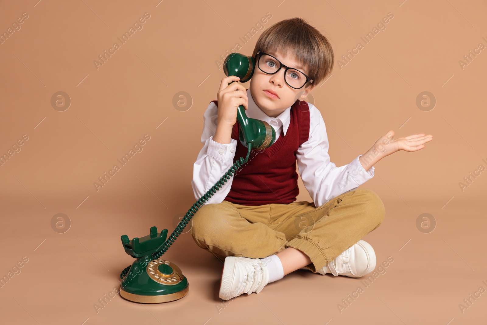 Photo of Cute little boy with old telephone on beige background