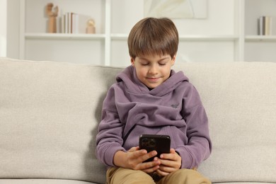 Cute little boy using smartphone on sofa at home