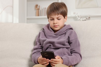 Photo of Cute little boy using smartphone on sofa at home