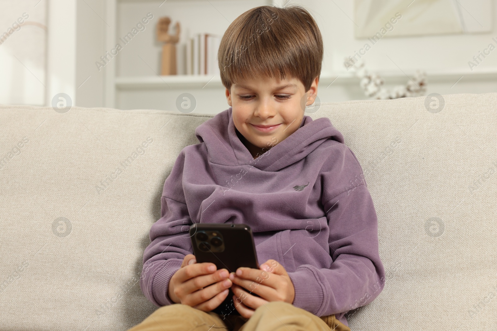 Photo of Cute little boy using smartphone on sofa at home