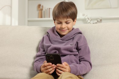 Cute little boy using smartphone on sofa at home