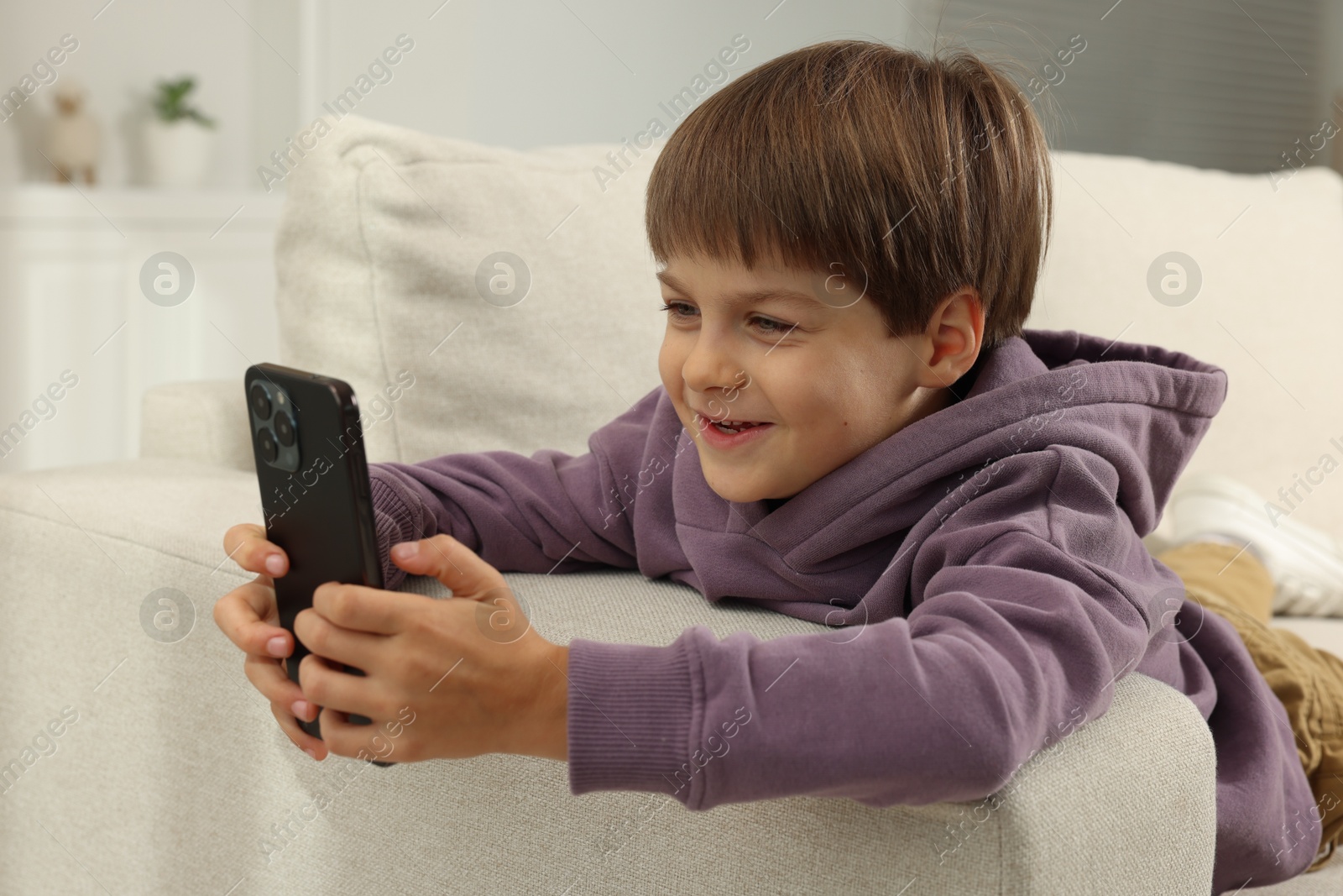 Photo of Cute little boy using smartphone on sofa at home