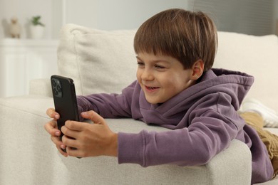 Cute little boy using smartphone on sofa at home