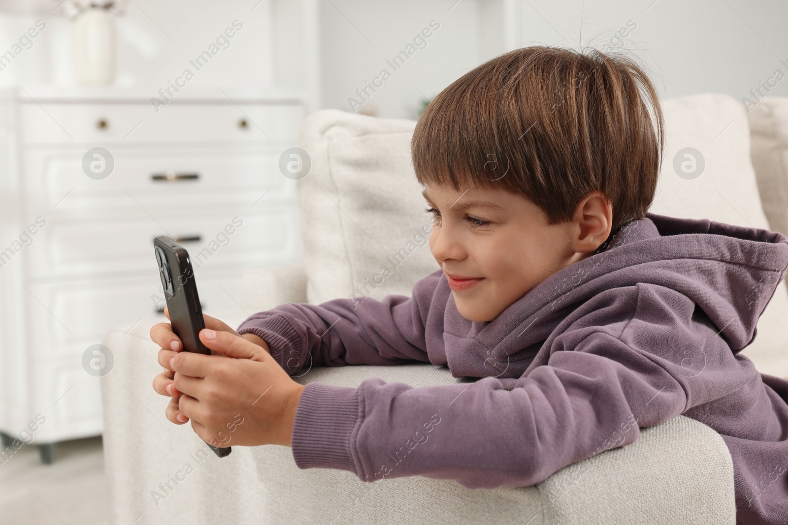 Photo of Cute little boy using smartphone on sofa at home