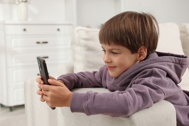 Cute little boy using smartphone on sofa at home