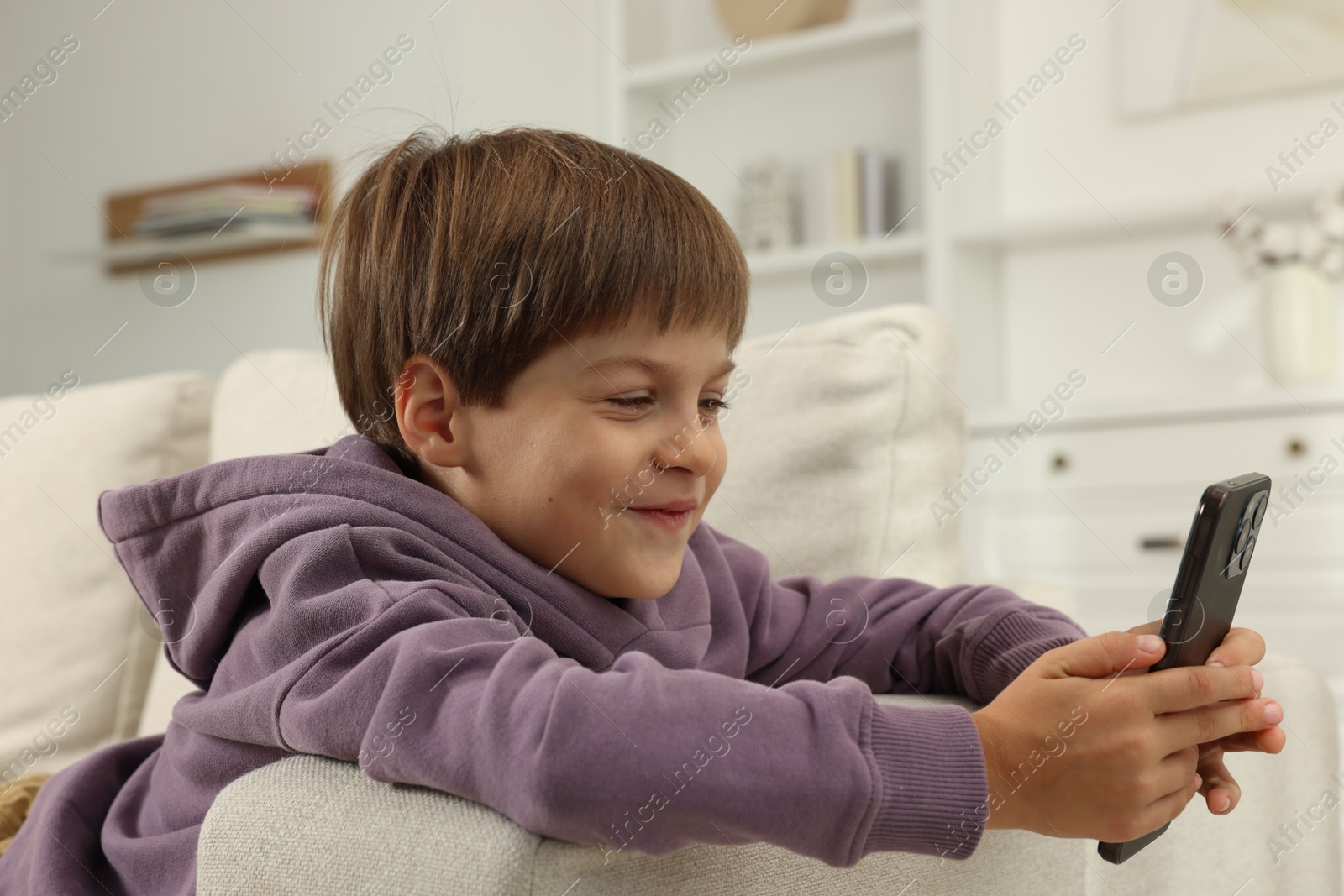 Photo of Cute little boy using smartphone on sofa at home