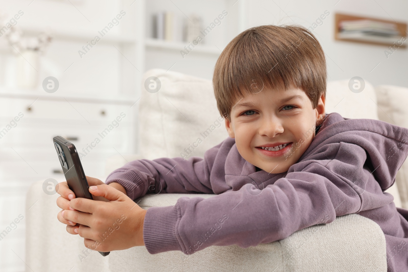 Photo of Cute little boy using smartphone on sofa at home