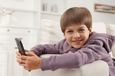 Cute little boy using smartphone on sofa at home