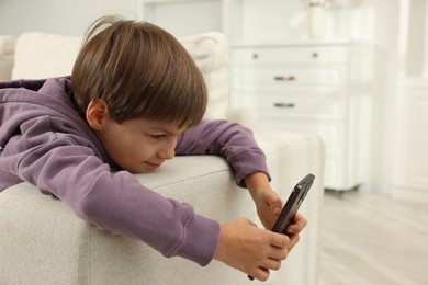 Cute little boy using smartphone on sofa at home