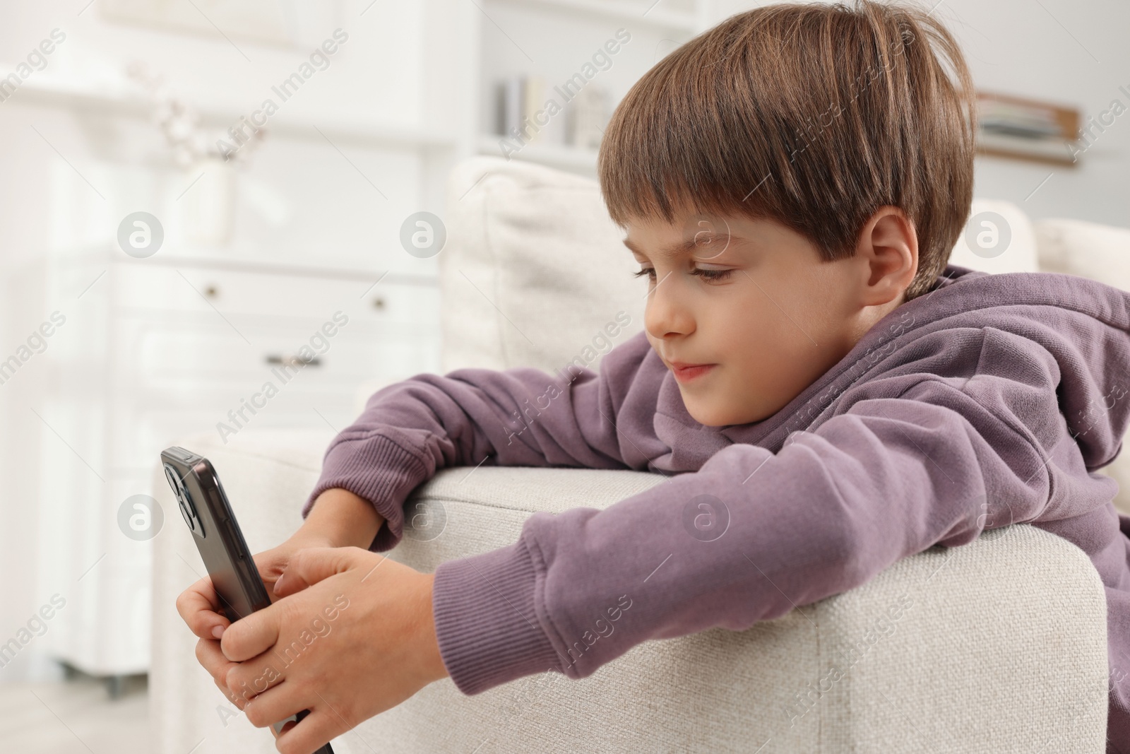 Photo of Cute little boy using smartphone on sofa at home