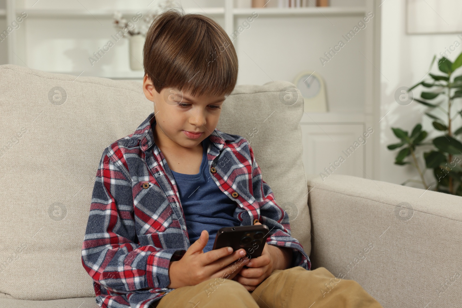 Photo of Cute little boy using smartphone on sofa at home