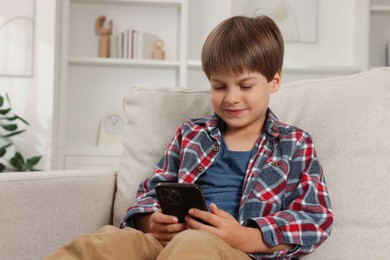 Cute little boy using smartphone on sofa at home