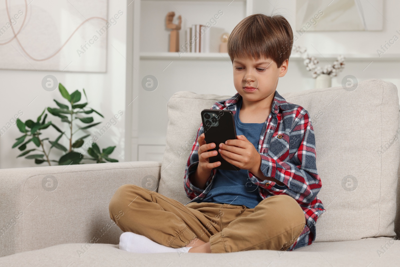 Photo of Cute little boy using smartphone on sofa at home