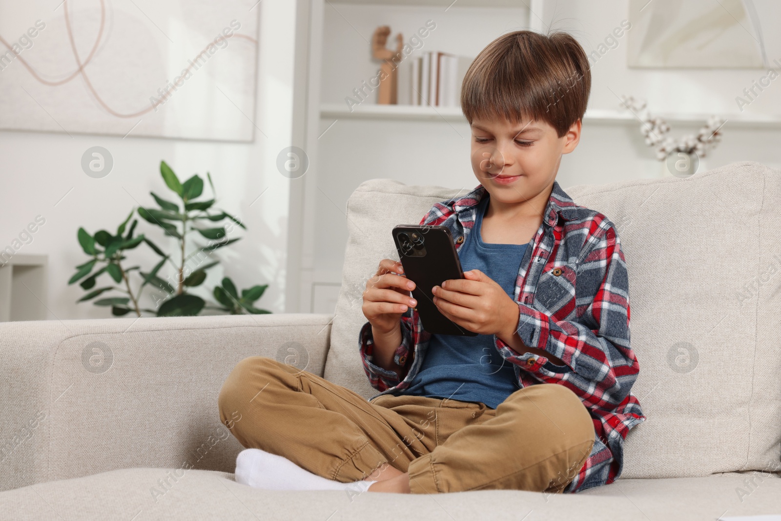 Photo of Cute little boy using smartphone on sofa at home