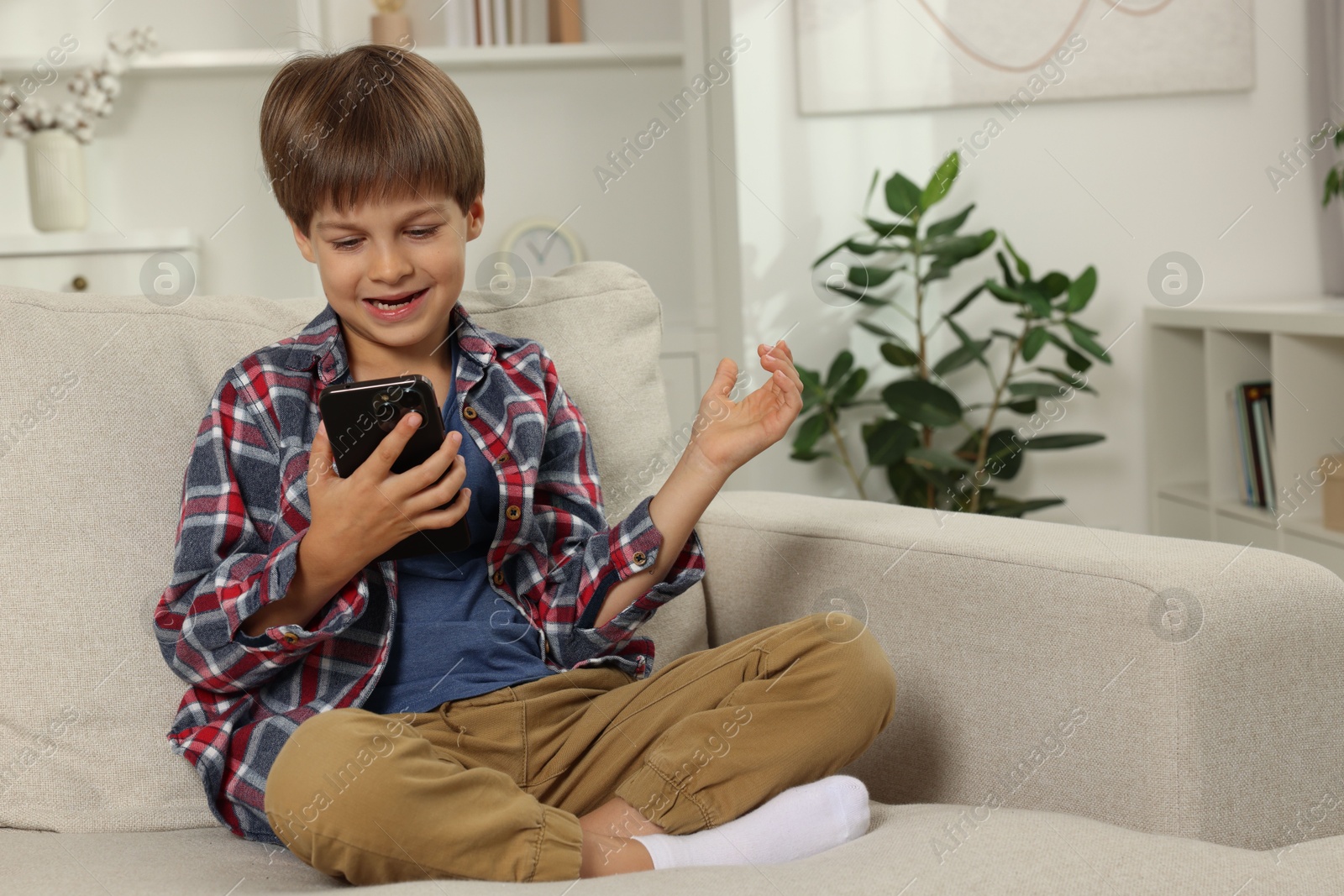 Photo of Cute little boy using smartphone on sofa at home