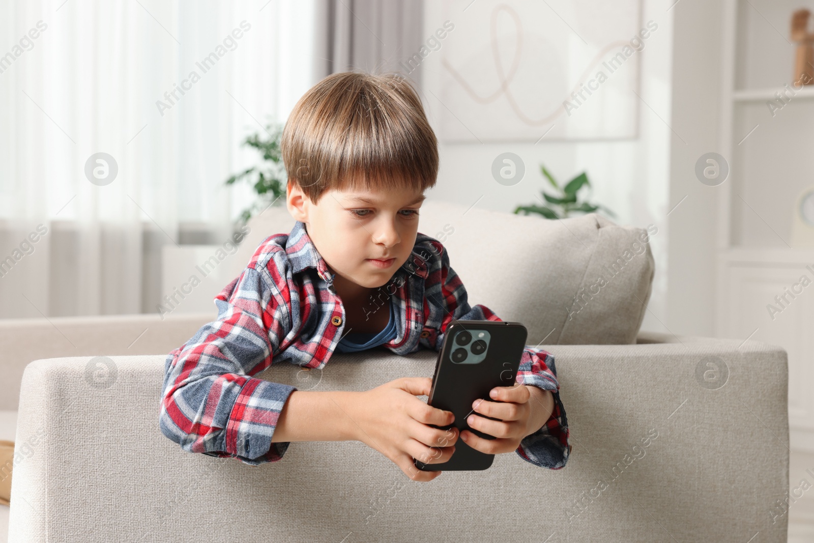 Photo of Cute little boy using smartphone on sofa at home