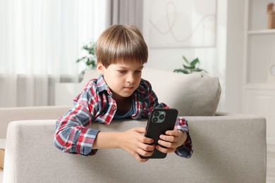 Cute little boy using smartphone on sofa at home