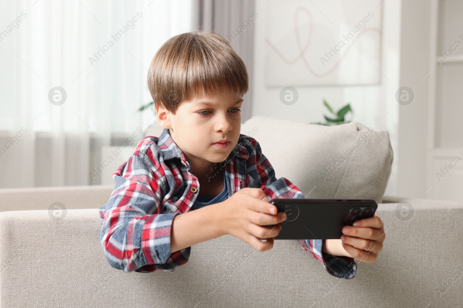 Photo of Cute little boy using smartphone on sofa at home