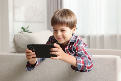 Cute little boy using smartphone on sofa at home