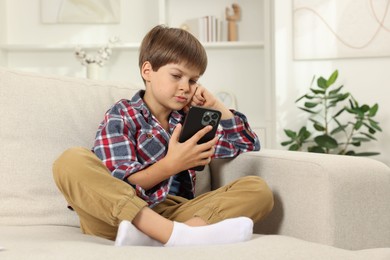 Photo of Cute little boy using smartphone on sofa at home