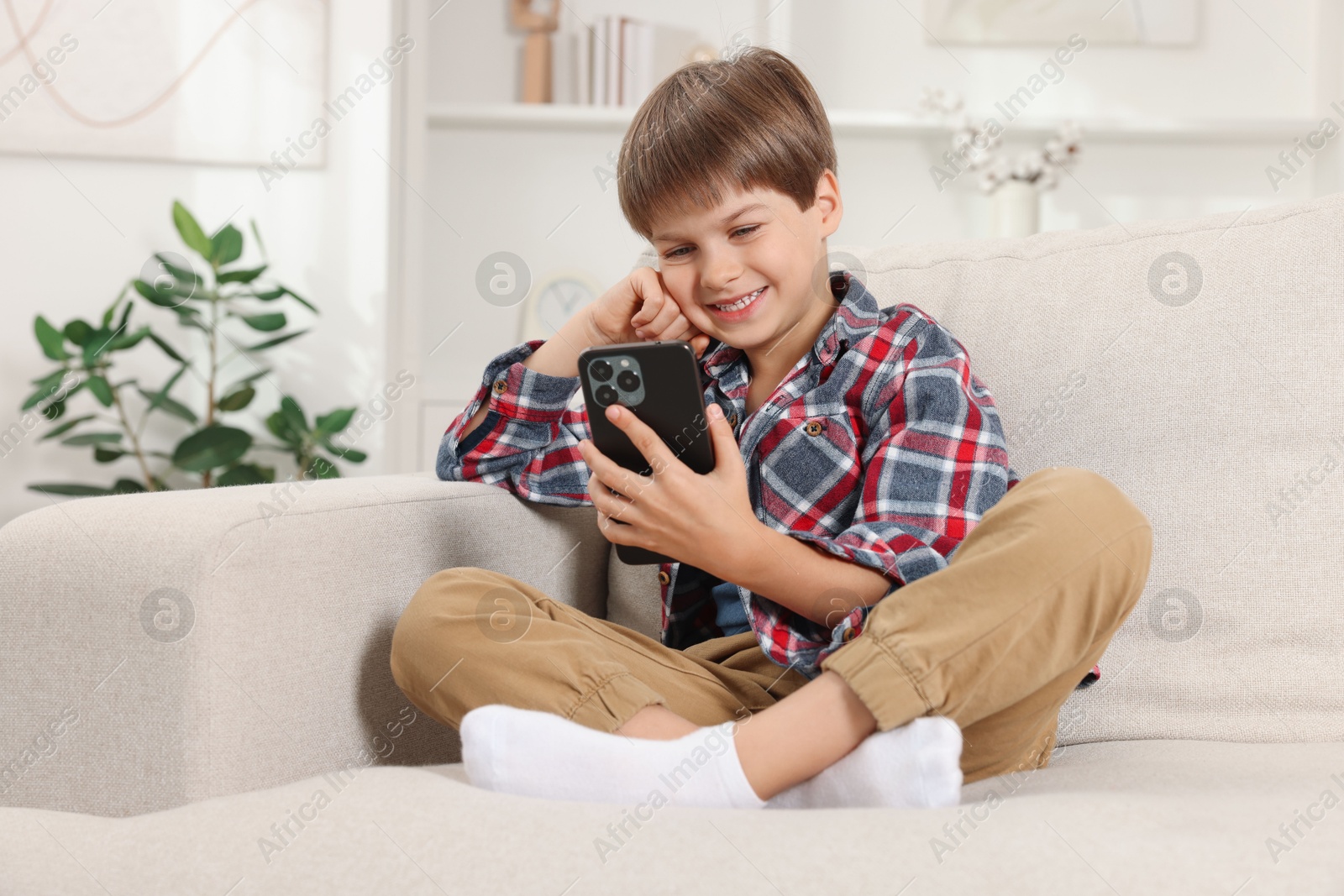 Photo of Cute little boy using smartphone on sofa at home