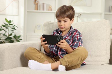 Cute little boy using smartphone on sofa at home