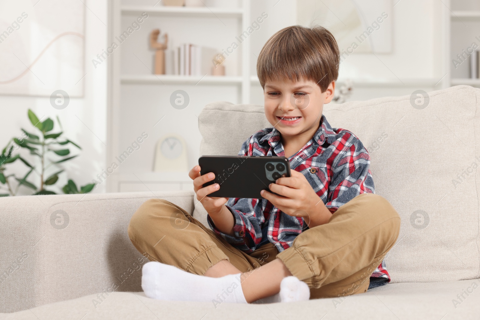 Photo of Cute little boy using smartphone on sofa at home