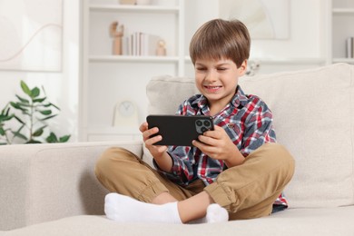 Cute little boy using smartphone on sofa at home