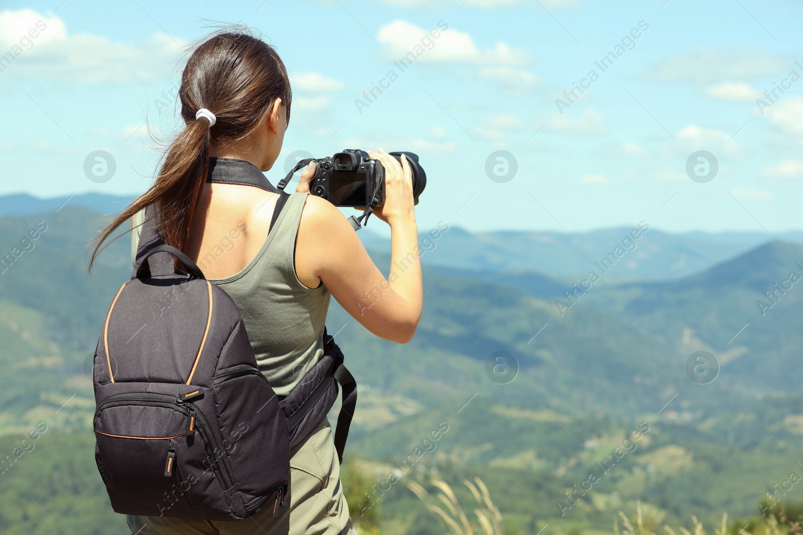 Photo of Photographer with backpack and camera taking picture of beautiful mountains, back view. Space for text