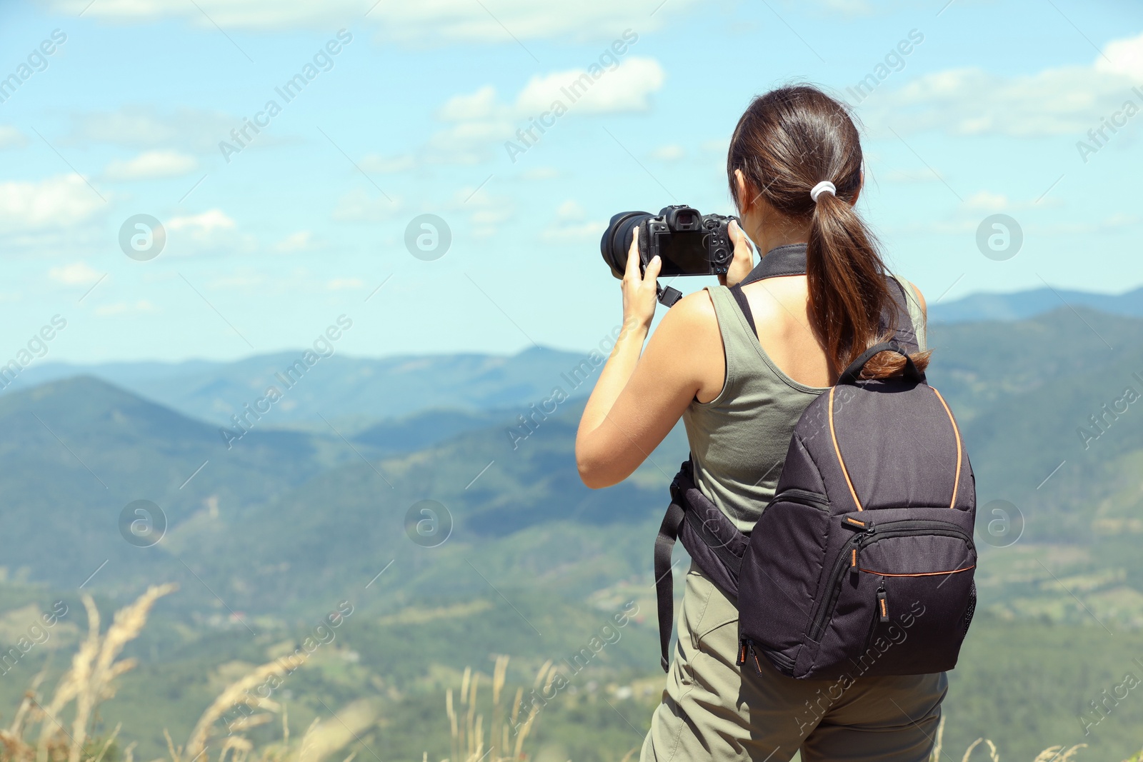 Photo of Photographer with backpack and camera taking picture of beautiful mountains, back view. Space for text