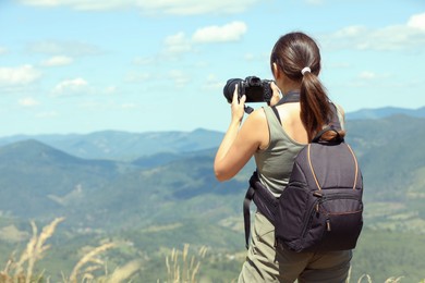 Photographer with backpack and camera taking picture of beautiful mountains, back view. Space for text