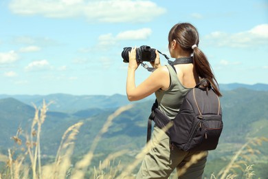 Photographer with backpack and camera taking picture of beautiful mountains, back view