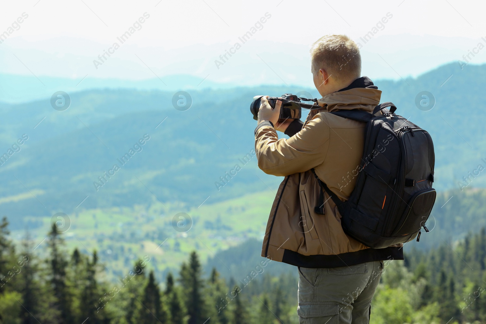 Photo of Photographer with backpack and camera taking picture of beautiful mountains, back view. Space for text