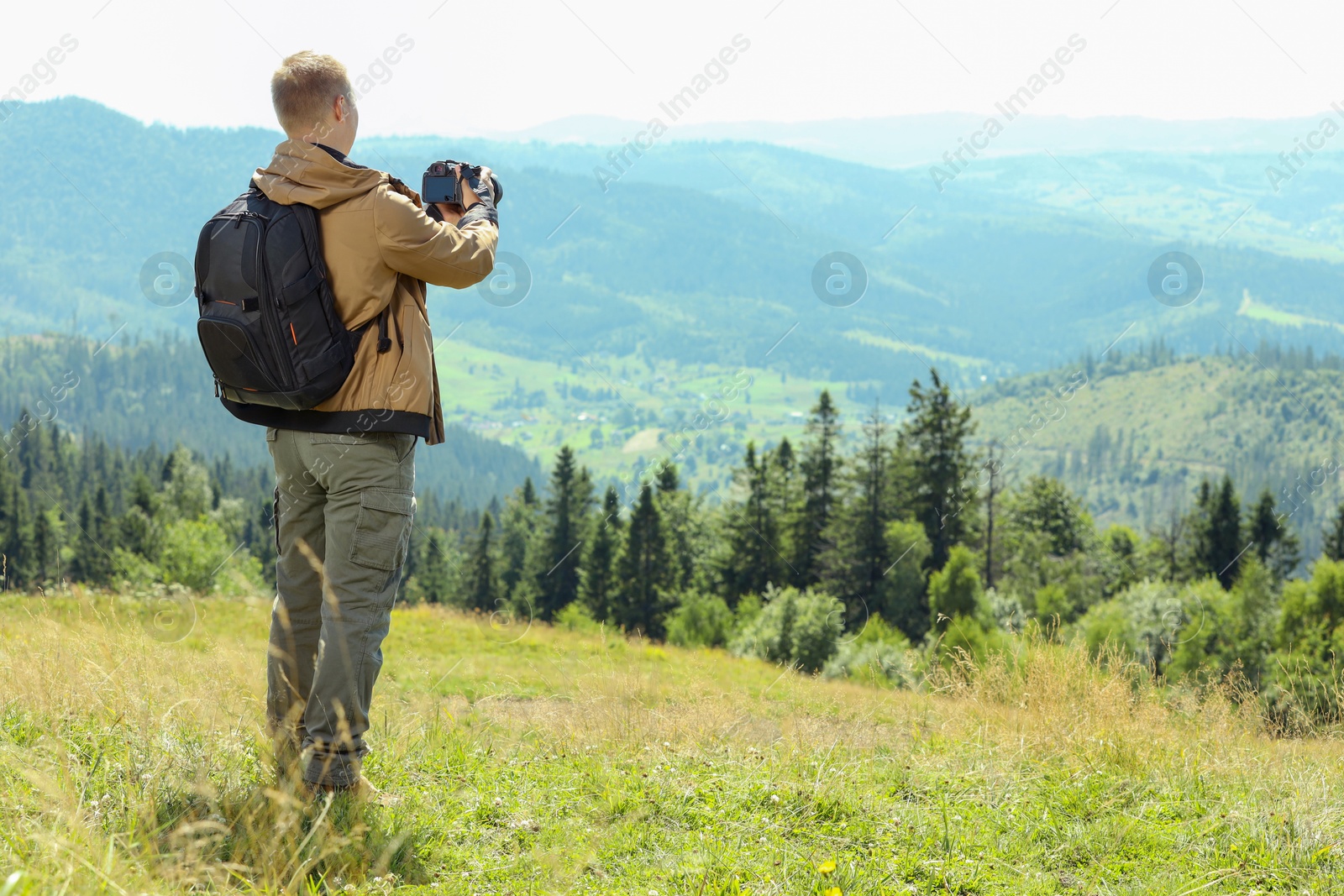 Photo of Photographer with backpack and camera taking picture of beautiful mountains, back view. Space for text