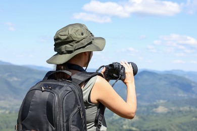 Photographer with backpack and camera taking picture of beautiful mountains, back view