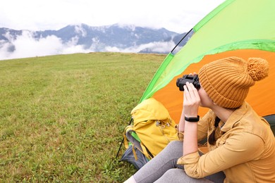 Young camper with binoculars and tent in mountains, space for text. Active tourism