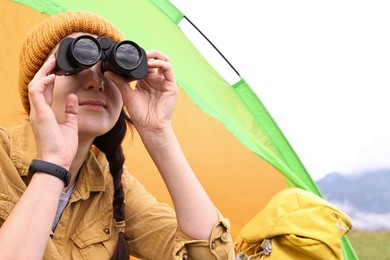 Young camper with binoculars and tent in mountains, space for text. Active tourism