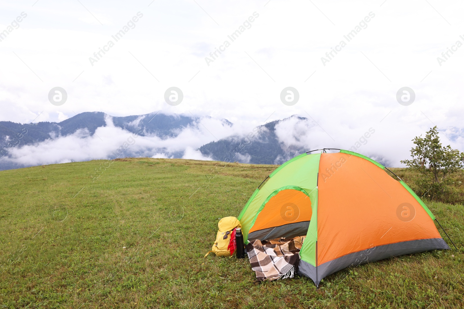 Photo of Tent, backpack and camping equipment on green grass in mountains, space for text