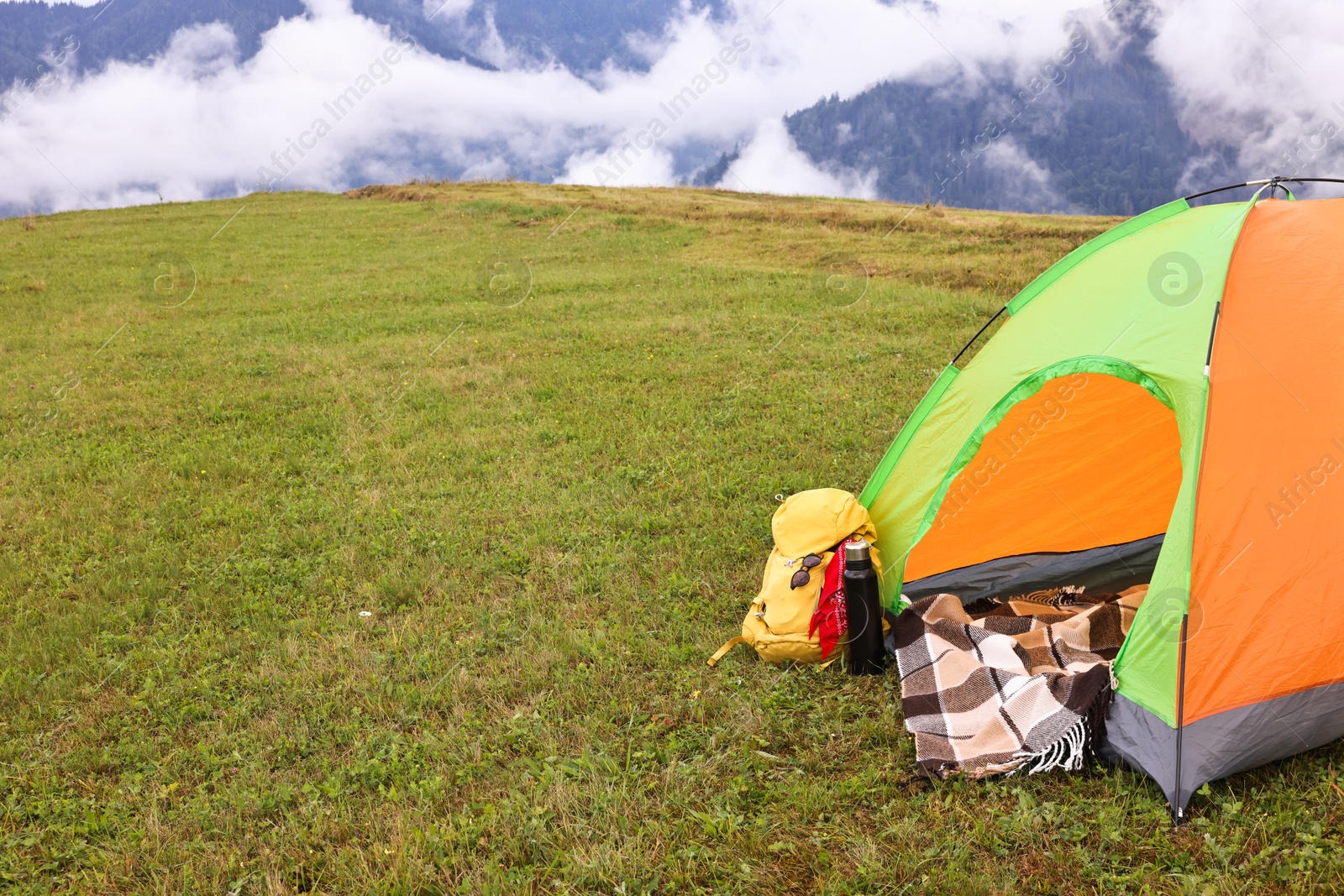 Photo of Tent, backpack and camping equipment on green grass in mountains, space for text