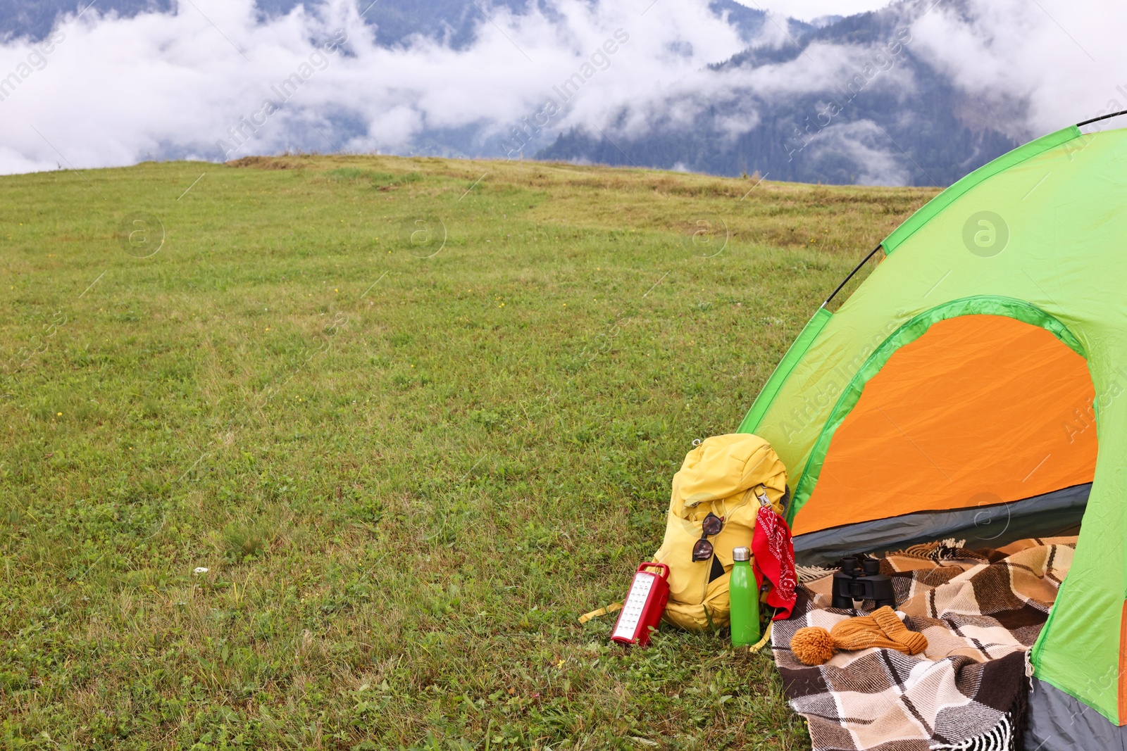 Photo of Tent, backpack and camping equipment on green grass in mountains, space for text