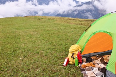 Photo of Tent, backpack and camping equipment on green grass in mountains, space for text