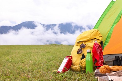 Tent, backpack and camping equipment on green grass in mountains, space for text