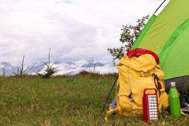 Tent, backpack and camping equipment on green grass in mountains, space for text