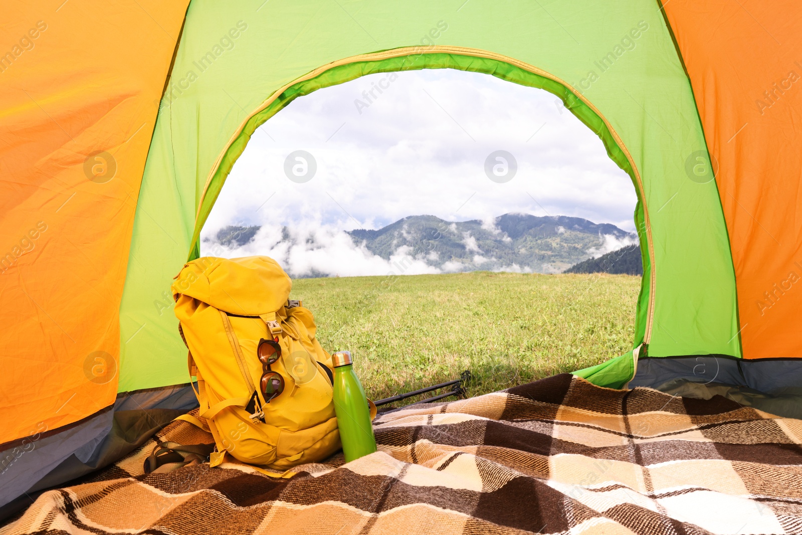 Photo of Tent, backpack and thermos on green grass in mountains