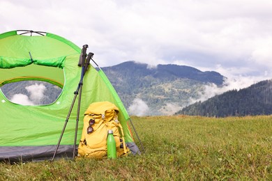 Photo of Tent, backpack, trekking poles and thermos on green grass in mountains, space for text