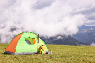 Tent, backpack, trekking poles and thermos on green grass in mountains, space for text