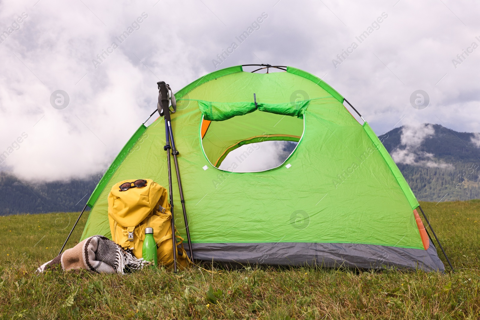 Photo of Tent, backpack, trekking poles and thermos on green grass in mountains