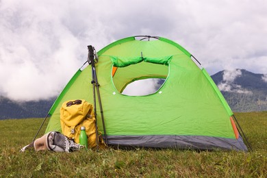 Photo of Tent, backpack, trekking poles and thermos on green grass in mountains