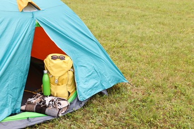 Photo of Tent, backpack, blanket and thermos on green grass outdoors, space for text